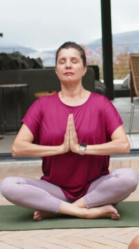 Vertical video: Praying, lady meditating, lowering hands to lap on patio, magenta top, green mat