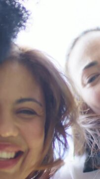 Vertical video: Leaning 2 women laughing talking into cam outside in red and white hand on shoulder