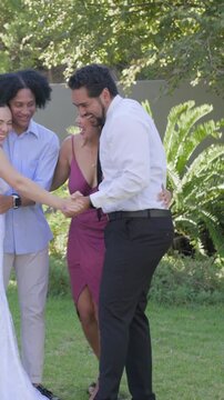 Linking hands after ceremony, bride in white gown and groom dancing to celebrate on garden lawn