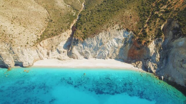Crystal clear water meets white sandy beach below towering cliffs on Kefalonia island in Greece