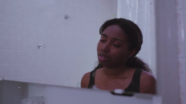 African American woman seen first in mirror reflection as camera pulls back toward her, examining skin closely with concern, expressing insecurity about appearance and facial imperfections