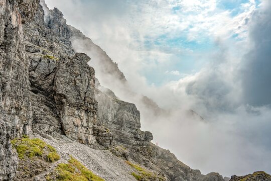 Spectacular Alpine Rock Face of Thaneller Mountain with Hiker in Red, Dramatic Clouds and Blue Sky over the Werner-Riezler-Steig Trail, High Altitude Adventure, Tyrol, Austria, Europe