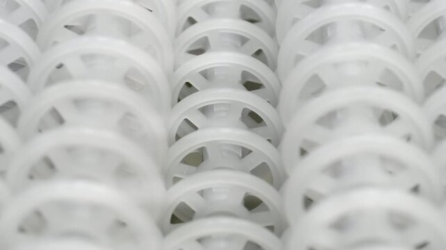 An industrial conveyor is in operation, white plastic rollers are rotating. Static handheld shot of production, sorting, or transportation line, real time speed, artificial lighting.