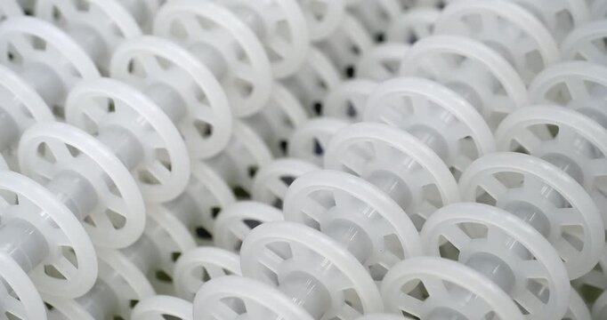 An industrial conveyor is in operation, white plastic rollers are rotating. Static handheld shot of production, sorting, or transportation line, real time speed, artificial lighting.