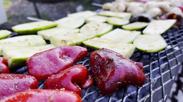 Vegetables roasting on home grill over open heat at summer day. Smoke rises gently as meal cook developing lightly charred surface. The focus on grilling process, texture and appetizing appearance