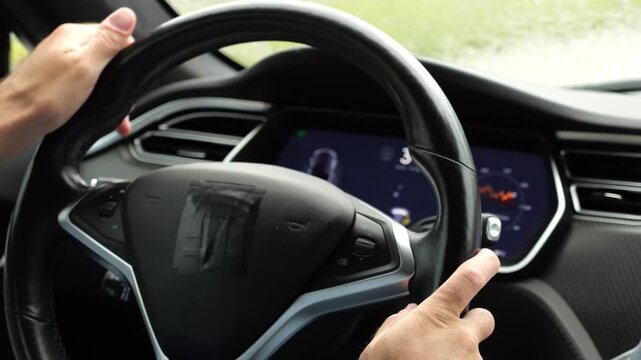 Male hands of businessman holds steering wheel while driving electrical vehicle at rain city. Young man commuting to work at rainy day. Businessperson operating electric car on urban road. Close up