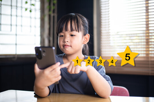 Young Asian girl using smartphone to give 5 star rating, customer satisfaction and online product feedback concept, little child interacting with mobile app.