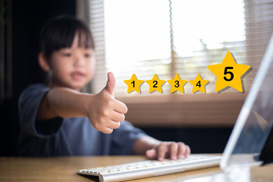 Smiling young Asian girl giving thumbs-up for 5-star rating after using computer