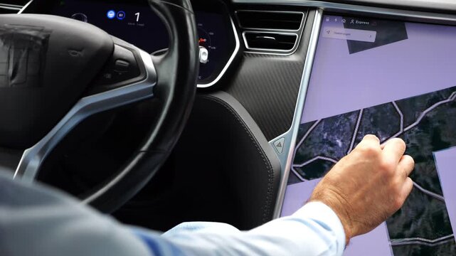 Male hand of businessman interacts with touchscreen of electric car displaying map. Close up shows modern vehicle interior and navigation technology, emphasizing digital lifestyle and smart mobility