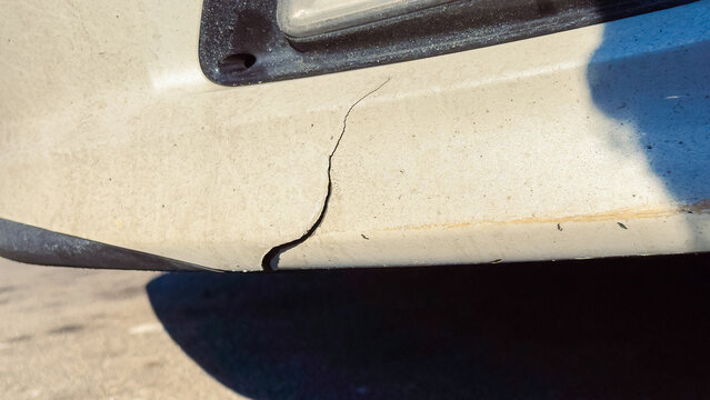 Crack seen on the bumper of a car parked on the street during daylight hours indicating damage to the vehicle