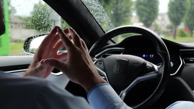 Young businessman experience to ride an autonomous self driving electric car at rainy day. Male businessperson resting during riding on electrical auto with autopilot at urban road. Slow motion