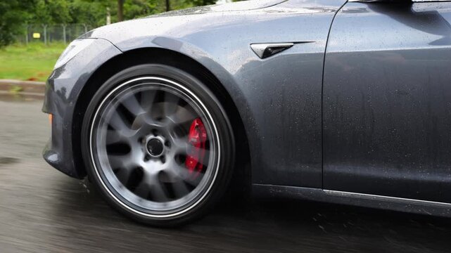 Wheel of modern electrical automobile driving at urban road on rainy day. Ecology friendly car riding moving along motorway. Electric vehicle riding through empty highway. Green innovation concept