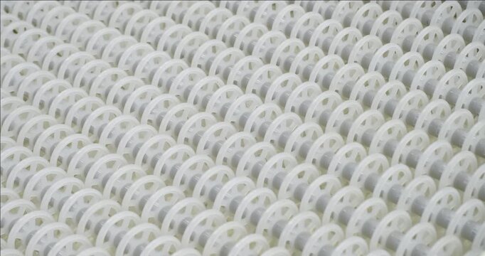 An industrial conveyor is in operation, white plastic rollers are rotating. Static handheld shot of production, sorting, or transportation line, real time speed, artificial lighting.