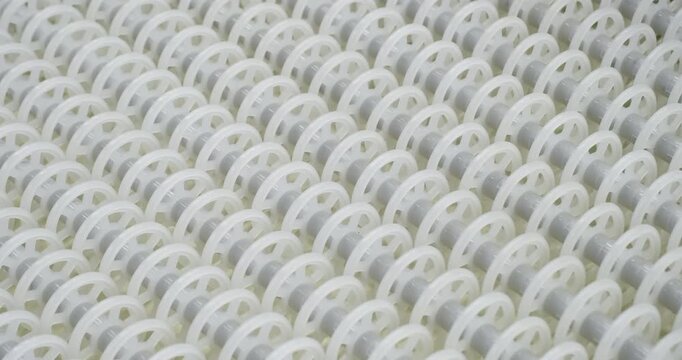 An industrial conveyor is in operation, white plastic rollers are rotating. Static handheld shot of production, sorting, or transportation line, real time speed, artificial lighting.