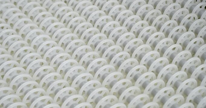 An industrial conveyor is in operation, white plastic rollers are rotating. Static handheld shot of production, sorting, or transportation line, real time speed, artificial lighting.