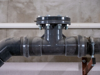 Fototapeta premium Industrial plastic pipe flange connection with bolts in building utility system. A close-up shot of a grey PVC or HDPE industrial pipe fitting with a flanged T-junction
