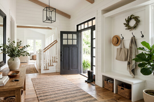 A modern farmhouse foyer with white walls, a built-in bench with coat hooks, an open front door, and view towards the stairs and living room.