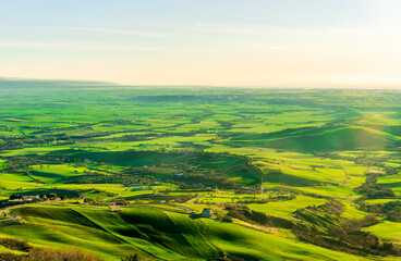 Obraz premium amazing panoramic landscape of green sunrise or sunset valley with farmland hills and rural fields and gardens with beautiful bright sunrise or sunset on background