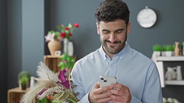 Man florist holding bouquet, smiling while looking at smartphone in studio; quiet contentment floral craft.