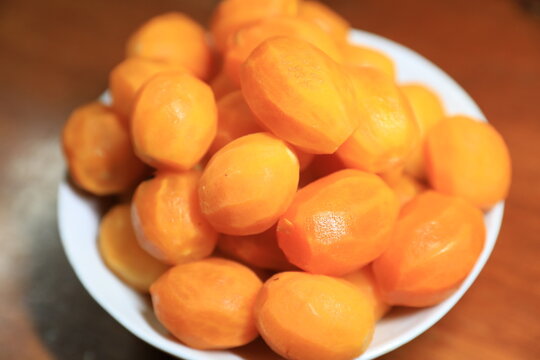 Fresh peeled Thai marian plums, also known as mayongchid or maprang, arranged in a white bowl on a wooden table. 