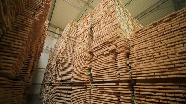 Detailed shot of lumber boards stacked together with a shallow depth of field and a blurred carpenter working in the background.