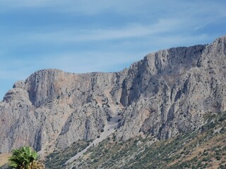 Fototapeta premium Majestic rocky cliffs of Sicilian landscape under a clear blue sky, showcasing the natural beauty of Sicily, Italy with lush greenery at the base