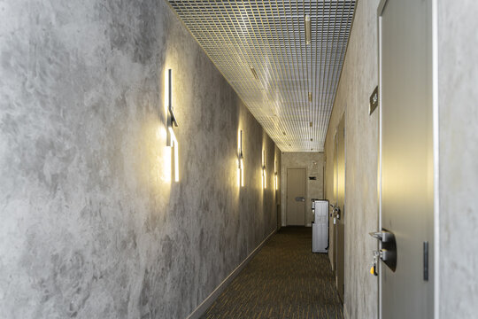 a long hallway with gray walls and light fixtures on the wall. hallway in apartment, house, hotel room. light walls, wooden doors. Modern flat. Hallway in stylish interior.  Architecture inside home