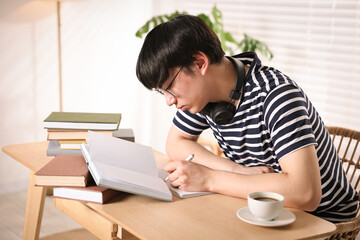 Fototapeta premium Student in glasses with headphones preparing for exam at wooden desk indoors