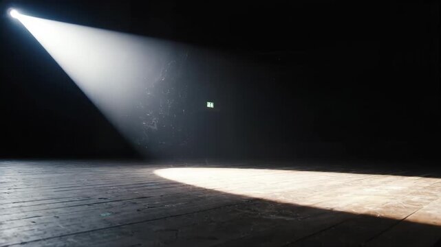 Bright white spotlight sweeping across a dark wooden stage floor. Dust particles floating in a moving light beam in an empty theater