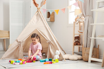 Little girl playing with building blocks near toy wigwam in playroom, space for text © New Africa