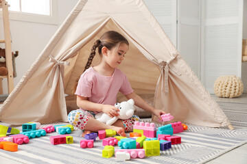 Little girl playing with building blocks near toy wigwam in playroom © New Africa