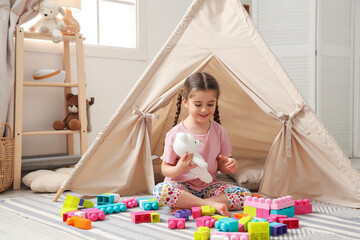 Little girl playing with building blocks near toy wigwam in playroom © New Africa