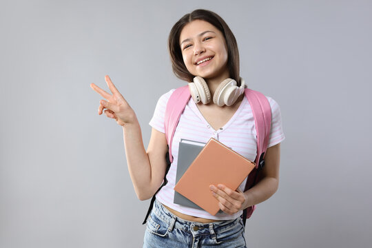 Teenage girl with notebooks showing peace sign on grey background