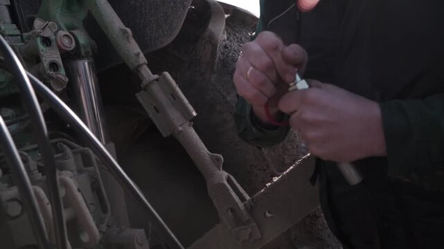 Farmer Connecting Grader Hydraulics to Tractor. Close view of farmer connecting hydraulic lines from grader to tractor