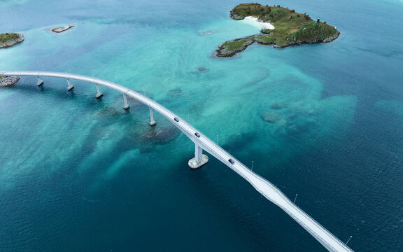 Aerial view of Sommaroy Bridge spanning across turquoise arctic waters with cars driving over it and small islands in Sommaroy, Troms, Norway.