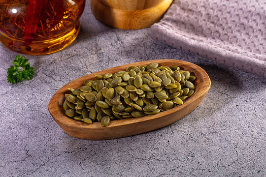 Peeled pumpkin seeds or pepitas in a wooden bowl on a rustic gray background