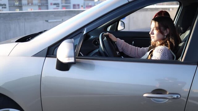 Young woman drives a car during practical lesson holding the steering wheel steady while instructor beside her gives directions and helps correct actions in real time