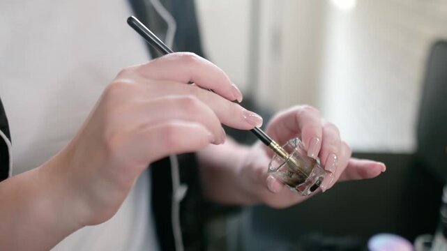 Beautician mixes color for eyebrows and eyelashes and prepares it for use. Closeup view of hands of makeup artist. Facial care and makeup in a professional salon.