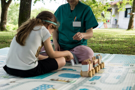 A healthcare worker in green uniform sits with a child on a play mat, facilitating an early intervention session focused on stimulation and growth.