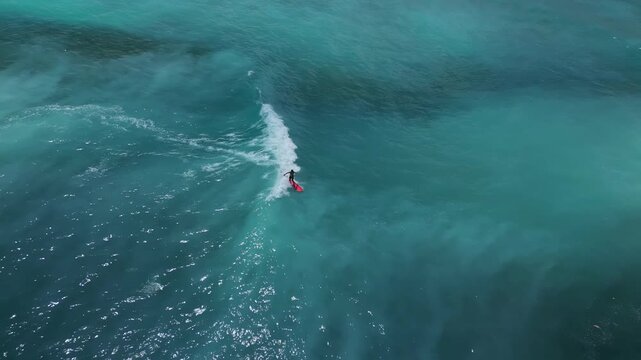 Aerial Shot Of Surfer Carving Turquoise Face. Dynamic Aerial View Of Surfer Maneuvering On Bright Red Board. Dramatic Drone Footage Showing Surfer Executing Sharp Turn Near Reef Obstacle, Java island