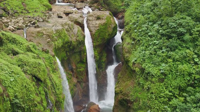 Top down aerial view of multi tier waterfall flowing through dense tropical rainforest in Costa Rica, cascading over moss covered rocks in lush green jungle landscape.