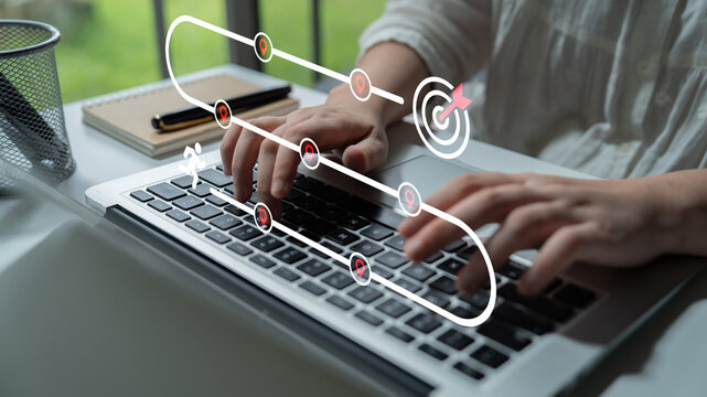 A woman types on a laptop in a modern office, surrounded by digital elements that represent goals and progress, symbolizing productivity and innovation in the workplace. Ledger