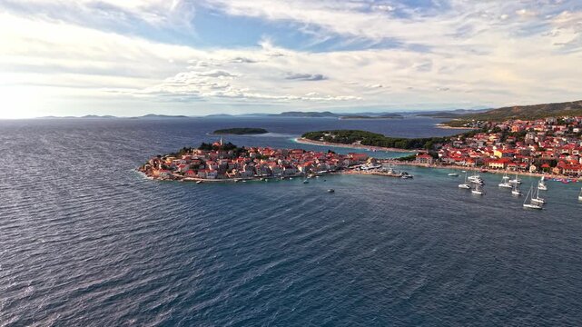 Aerial view of Primosten old town on the Adriatic coast in Croatia, featuring red-roofed houses, blue sea, and boats in the harbor