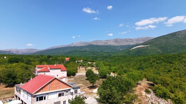 Aerial view of houses with red roofs in the rural landscape Croatia, with mountain range in the background under a clear blue sky