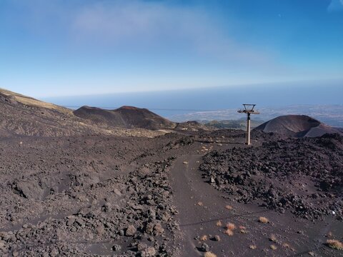 Mount Etna landscape featuring volcanic terrain, rocky paths, and a ski lift against a clear blue sky in Sicily, Italy, showcasing the natural beauty of an active stratovolcano