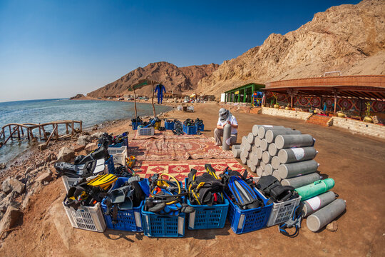 Professional dive master preparing scuba tanks and equipment on a beach for a diving excursion.

