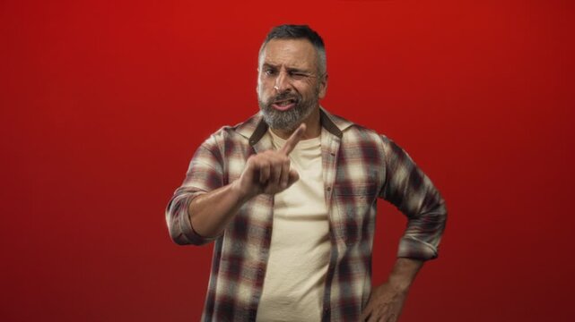 Man showing hands raised, pointing finger and open palms in red studio; frustration warning admonition stern.