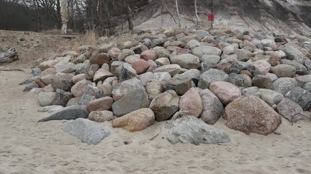 Large boulders and granite rocks on sandy beach used for coastal storm protection, ravine and natural gorge visible in background, elevation change and cliff height difference