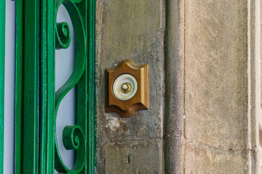 Vintage doorbell on stone wall beside green iron gate