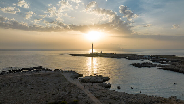 Aerial view of the Punta Sottile Lighthouse on the rocky coast at sunset with golden sun rays over the Mediterranean Sea in Favignana, Sicilia, Italy.